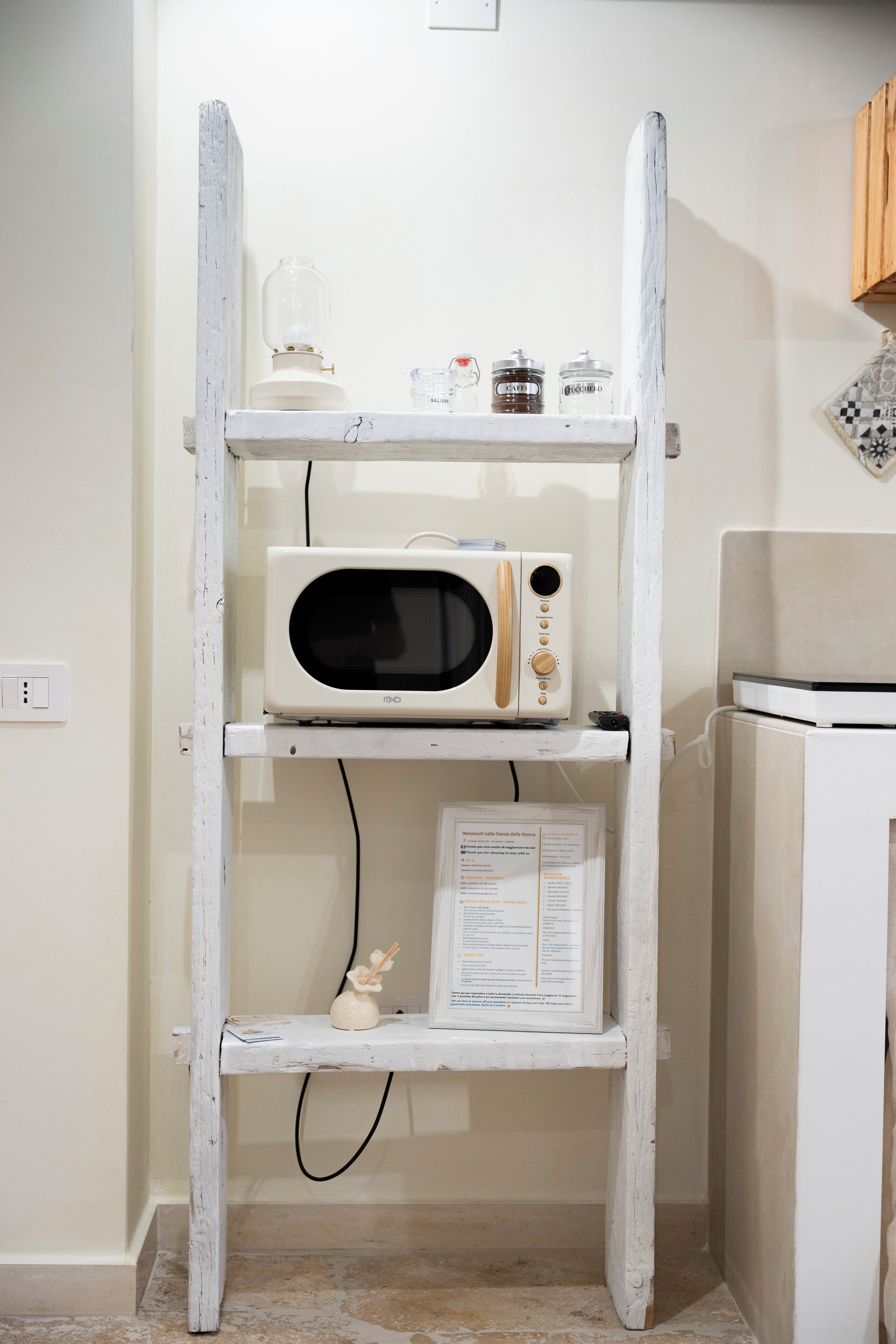 Une cuisine avec un micro-ondes blanc posé sur une étagère, un petit meuble et un réfrigérateur.