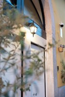 Una puerta con una lámpara encima, una cámara de seguridad instalada en la pared y una cesta colgante con flores.