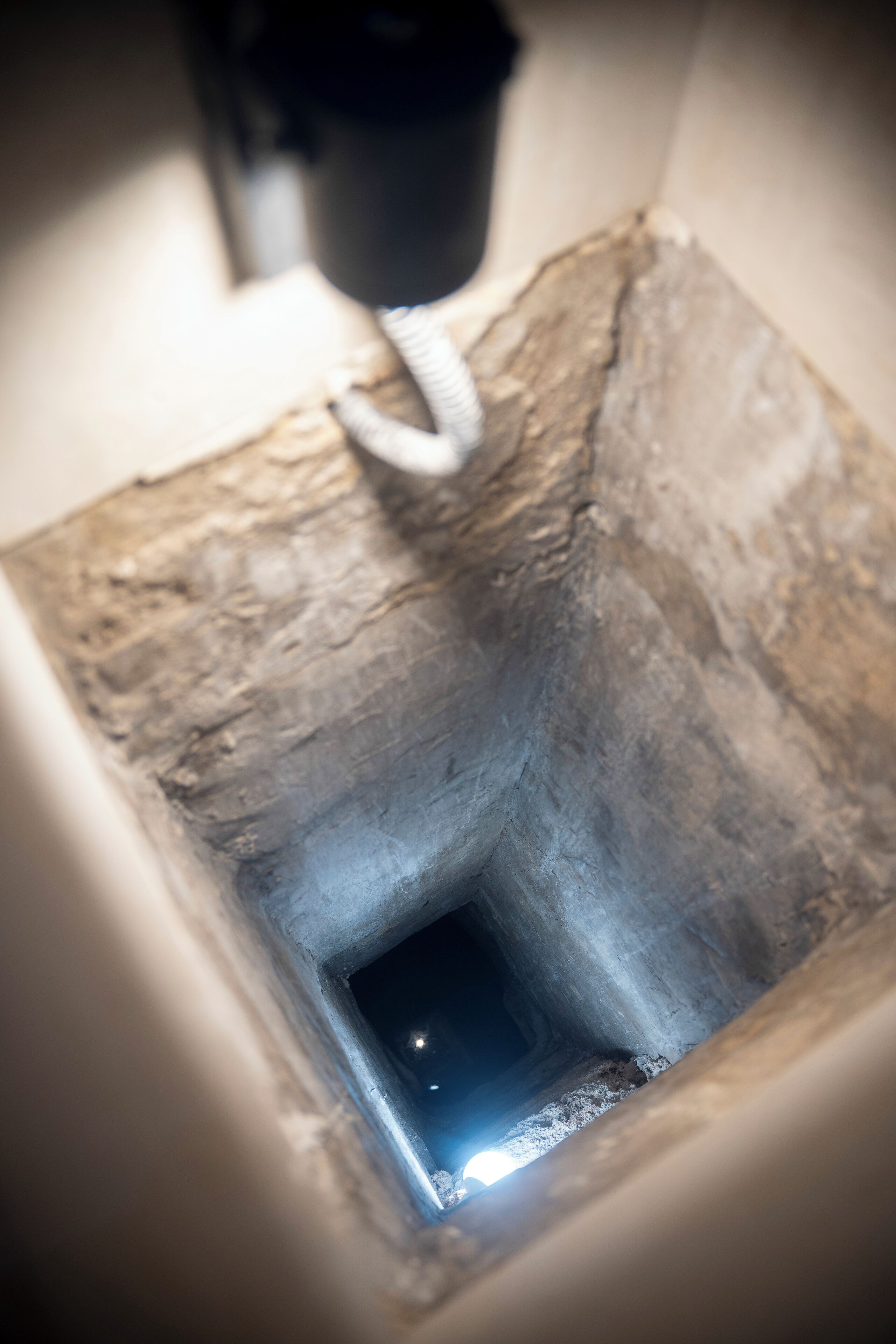 Eine schmale, schwach beleuchtete Treppe mit rauen, strukturierten Wänden und einer kleinen, beleuchteten Öffnung unten.
