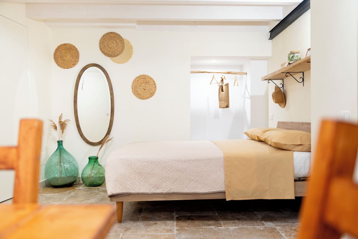 A bedroom with a bed, two green vases, a mirror, and woven wall decorations.