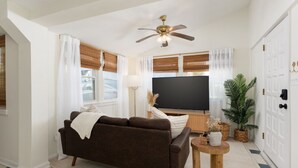 A living room with a brown sofa, a TV, a ceiling fan, and a potted plant.