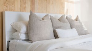 A neatly made bed with white bedding and multiple pillows in a room with wooden paneling on the wall.