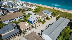 An aerial view of a coastal residential area with houses, a beach, and a pier in the background.