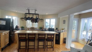 Een keuken met een centraal eiland, houten kastjes, een koelkast en een zithoek met een bank en stoelen.