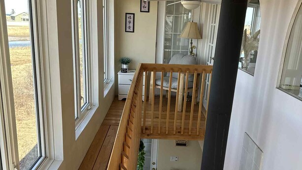 Een houten terras met een balustrade, een plafondventilator en uitzicht op een huis door grote ramen.
