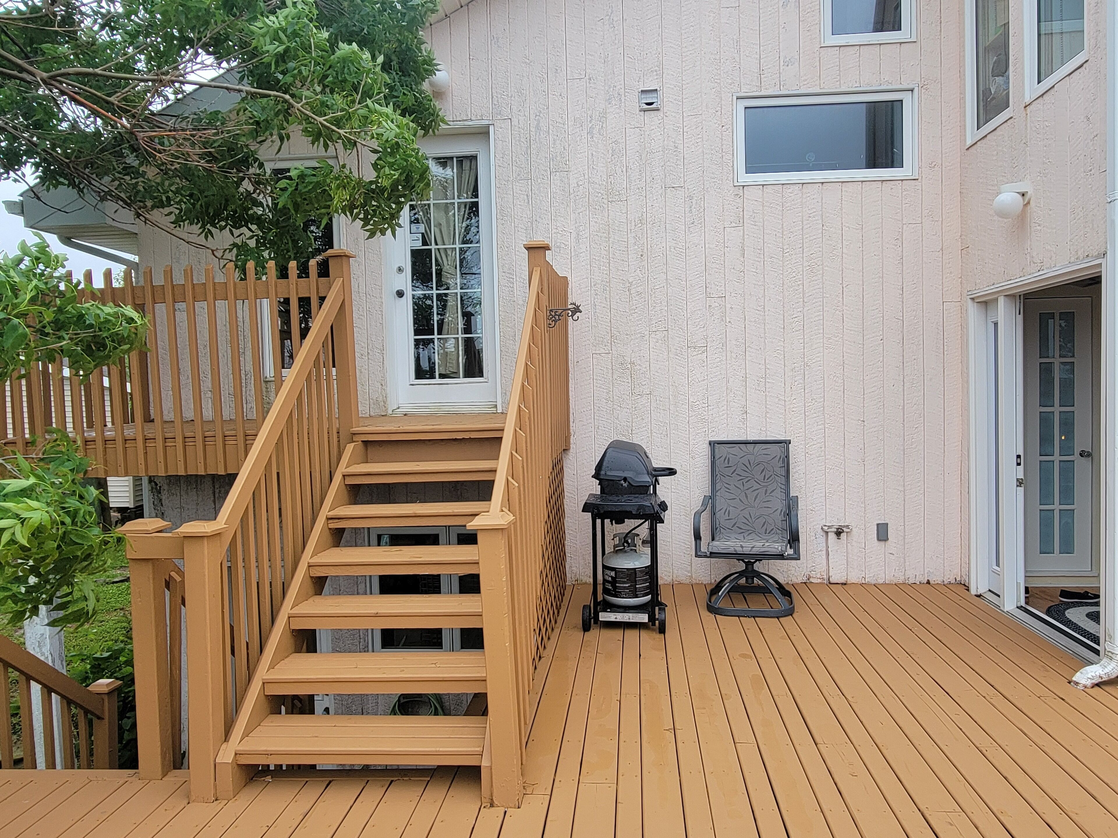 Eine Holzterrasse mit Treppe zu einer Tür, einem Grill und einem Stuhl.
