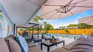 Ein Außenbereich mit Sofas, Sesseln, einem Pool und Sonnenschirmen.