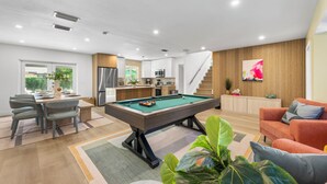 Ein modernes Wohnzimmer mit Billardtisch, Essbereich und einer Küche im Hintergrund.