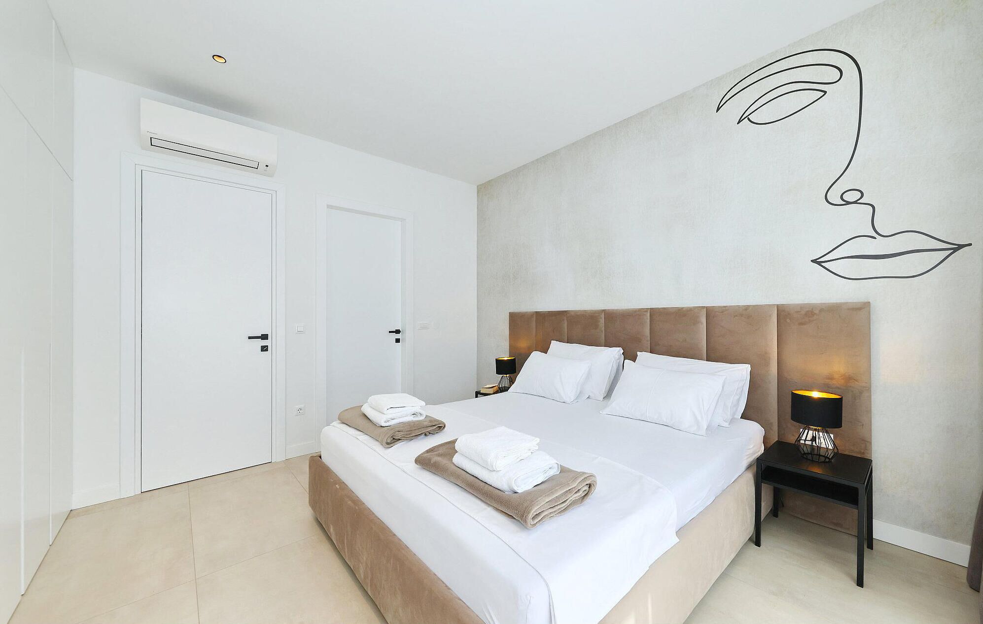 Una habitación de hotel moderna con una cama grande, cabecera, mesita de noche y una obra de arte en la pared.