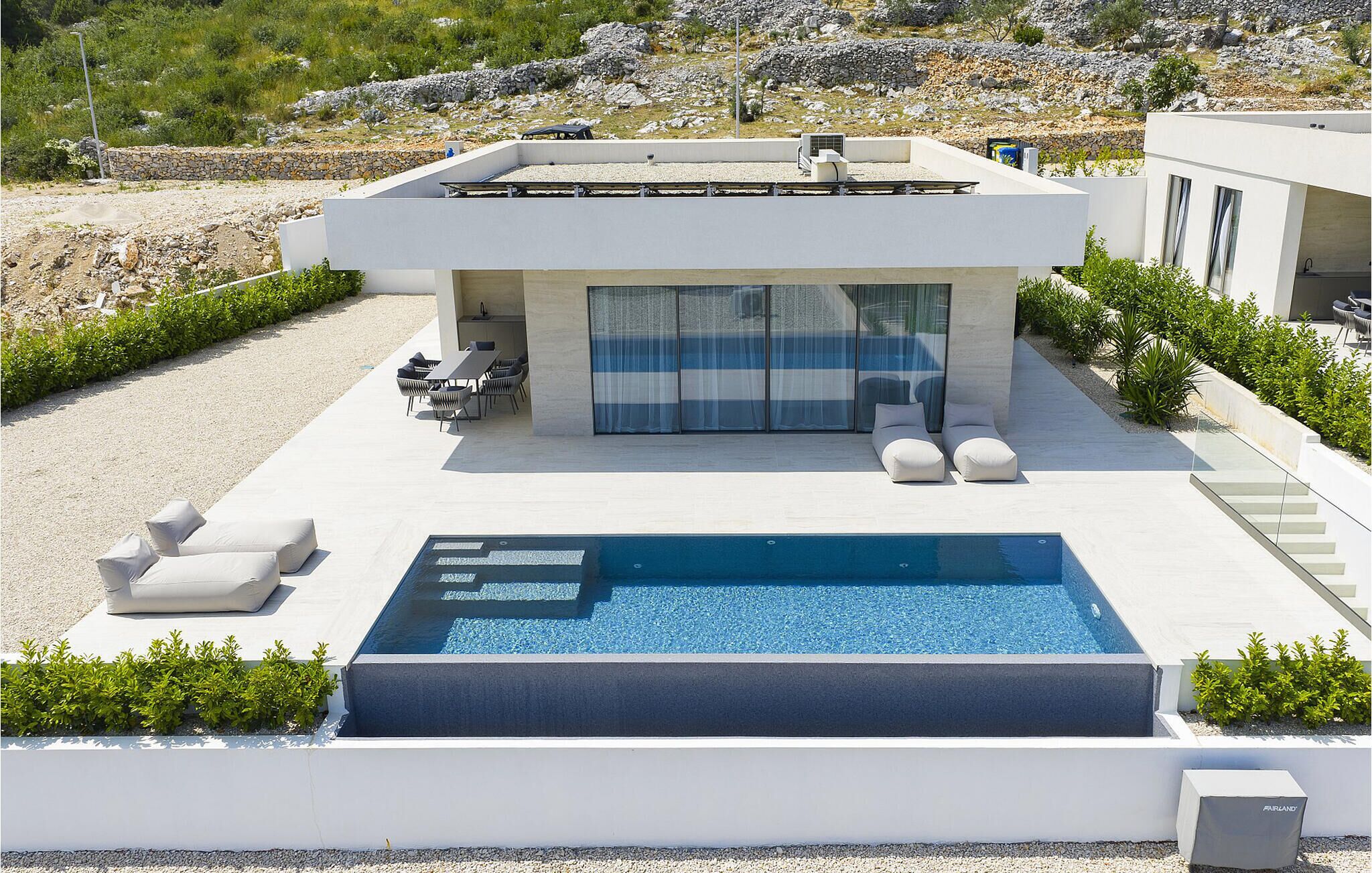 A modern house with a swimming pool, outdoor seating, and a view of the surrounding landscape.