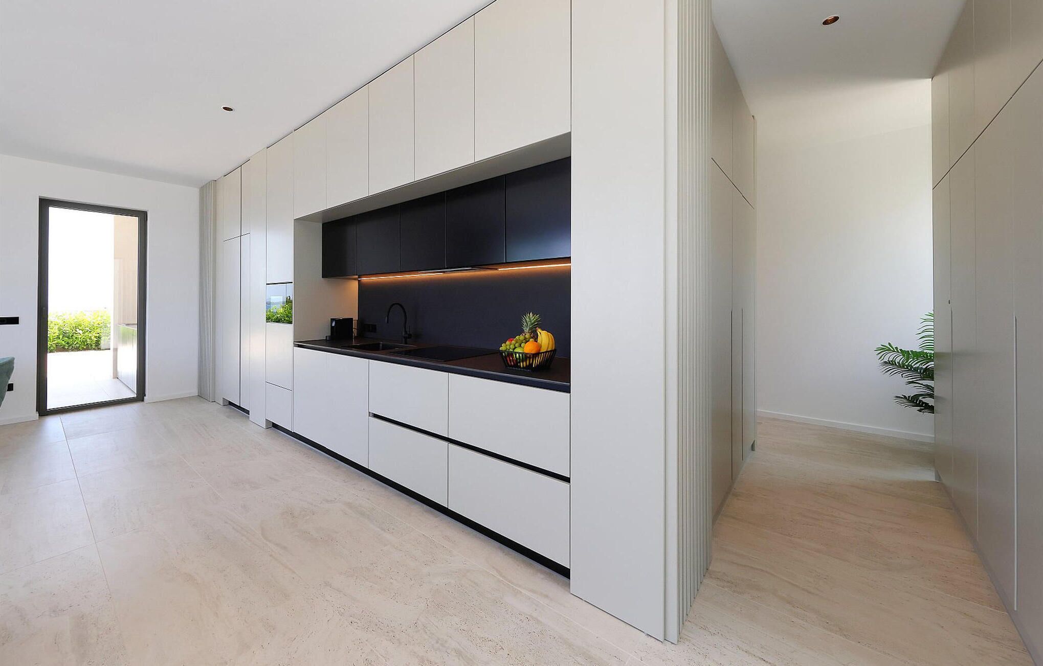 A modern kitchen with white cabinetry, a black countertop, and a fruit bowl.