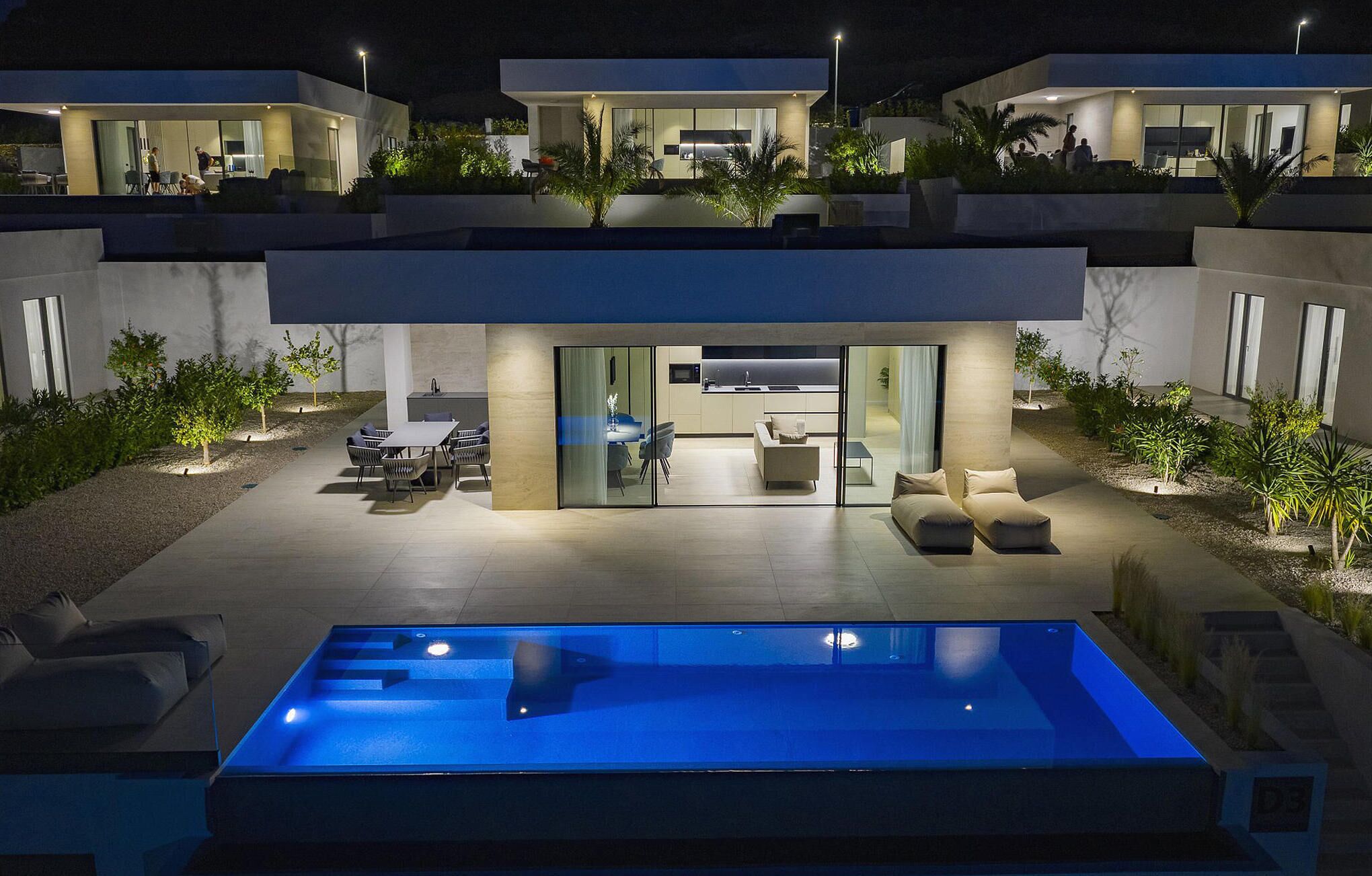 A modern house with a swimming pool, outdoor seating, and a kitchen visible through glass doors.