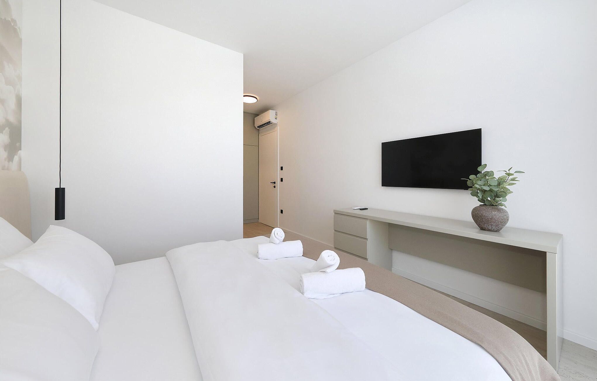 Quarto de hotel moderno com uma cama grande, televisão de tela plana na parede, uma pequena mesa com planta em vaso e um closet espaçoso.