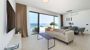 Un soggiorno moderno con divano, tavolino e zona pranzo con sedie. Grande finestra con vista sul mare.