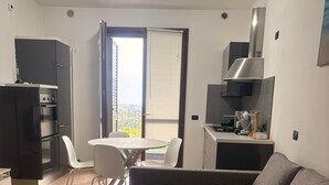 Eine moderne Wohnung mit einer Küchenzeile, einem Essbereich mit Tisch und Stühlen, einem grauen Sofa und einer Glastür zum Balkon.
