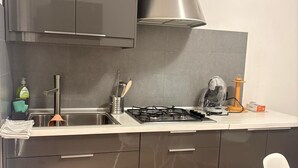 Eine moderne Küche mit dunklen Schränken, einer Edelstahl-Dunstabzugshaube, einem Gasherd und einem weißen Stuhl.