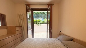 Ein Schlafzimmer mit Bett, Fenster und einer offenen Tür, die auf einen Balkon führt.