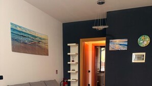 Ein modernes Wohnzimmer mit einem runden weißen Tisch, zwei weißen Stühlen, einem grauen Sofa und einem Bücherregal an einer dunklen Wand.