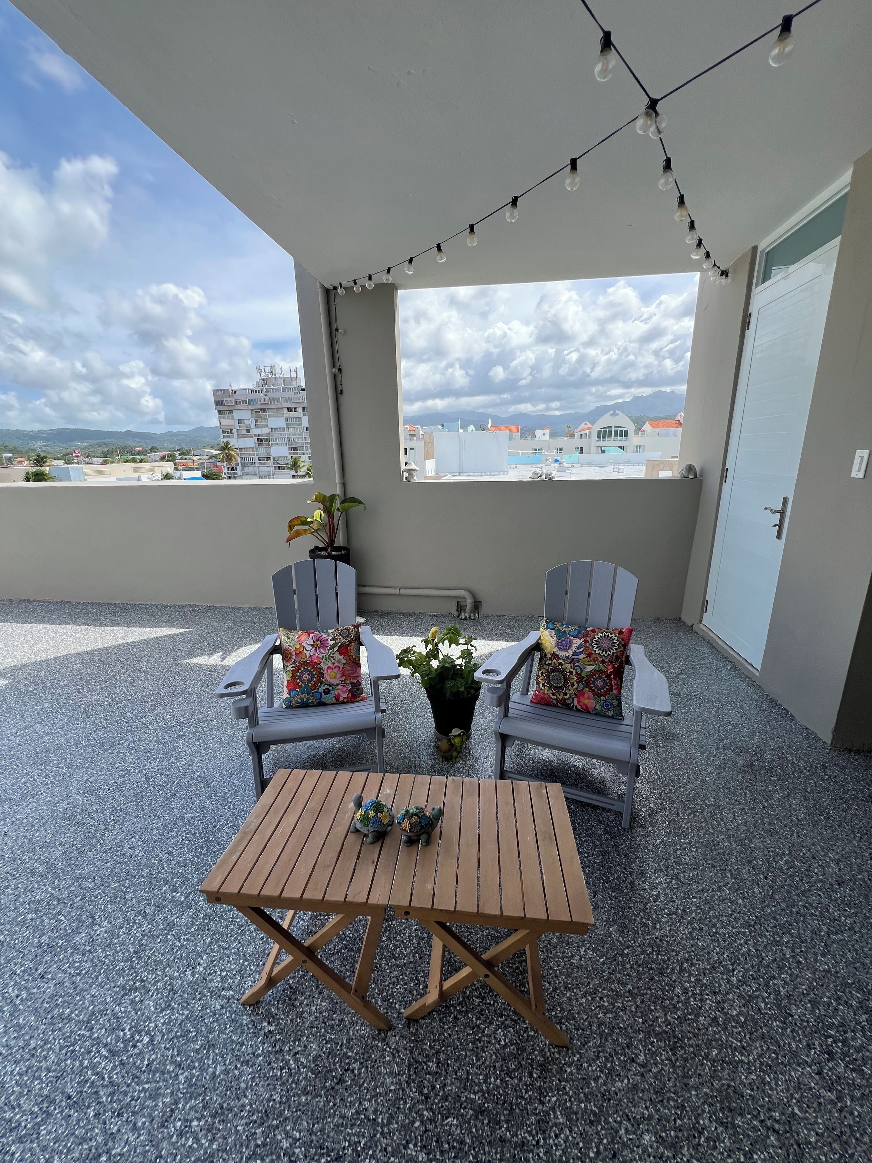 Un balcon avec deux chaises et une table, une plante en pot et des guirlandes lumineuses.