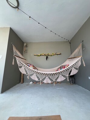 A hammock suspended between two walls, a string of lights above, and a branch with flowers on the wall.