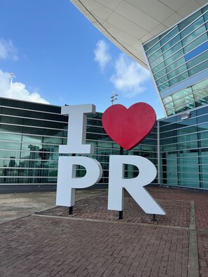 A large outdoor sign with the letters 'I' and 'PR' and a red heart symbol, set against a modern building with glass windows.
