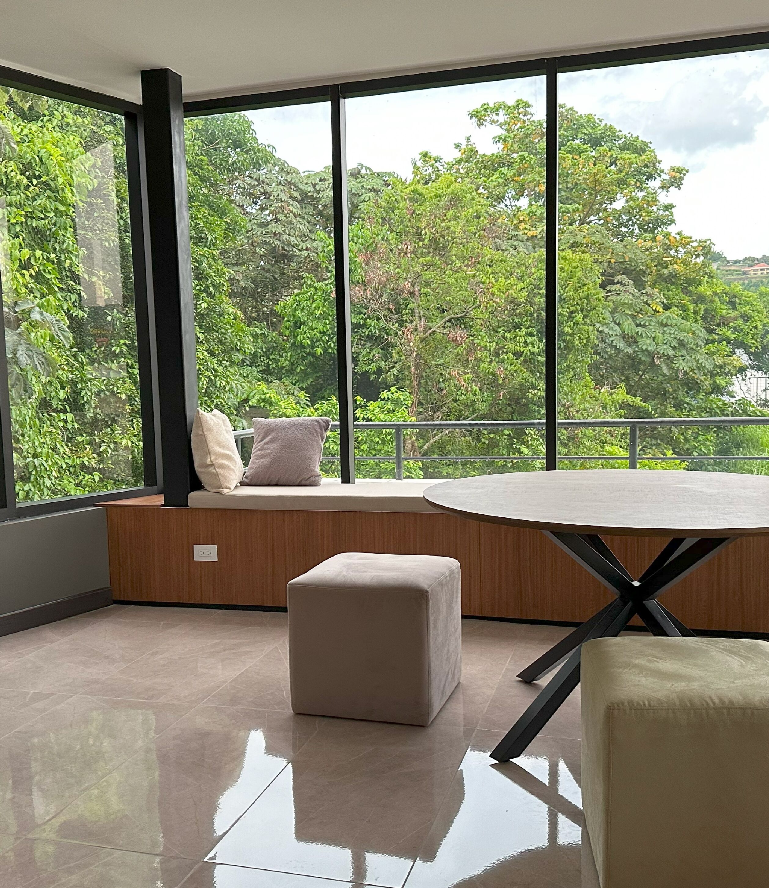 Ein modernes Zimmer mit großem Fenster, einem runden Tisch und einer Sitzecke mit Kissen.
