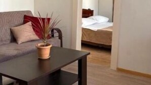 Ein Zimmer mit dunklem Holztisch, grauem Sofa mit roten Kissen und einem Bett mit weißer Bettwäsche.