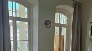 Ein Zimmer mit einem runden Tisch, zwei Stühlen und großen Fenstern mit Vorhängen.