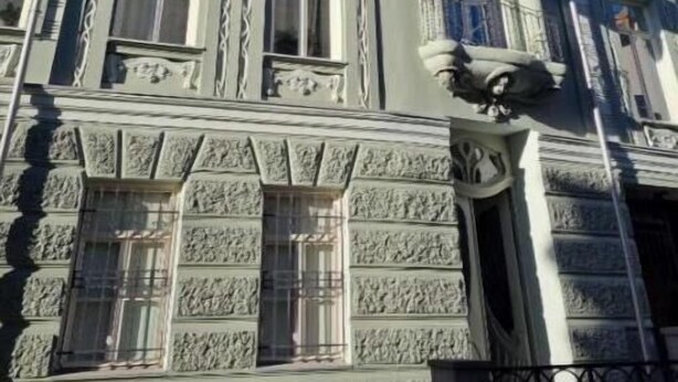 Ein Gebäude mit aufwendigen architektonischen Details, darunter dekorative Gesimse und ein Balkon mit schmiedeeisernem Geländer.