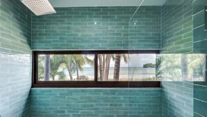 A bathroom with teal tiles and a window overlooking a beach with palm trees. - The Sanctuary - Luxury Beachfront 6-Bedroom Villa with 2 Swimming Pools (Playa Flamingo)