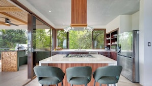A modern kitchen with a large island, three bar stools, and a view of the outdoors. - The Sanctuary - Luxury Beachfront 6-Bedroom Villa with 2 Swimming Pools (Playa Flamingo)