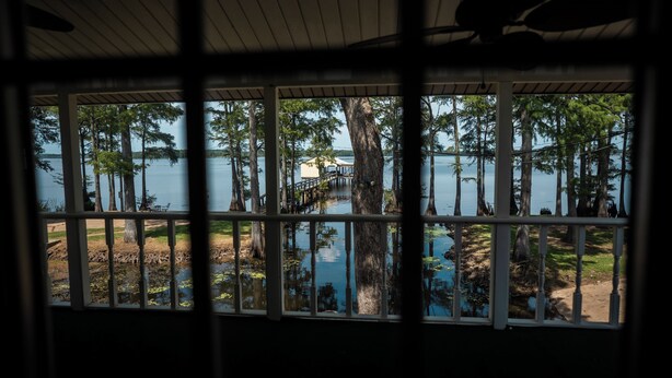 Une vue à travers une fenêtre à cadre en bois, donnant sur un lac bordé d’arbres et sur un quai.