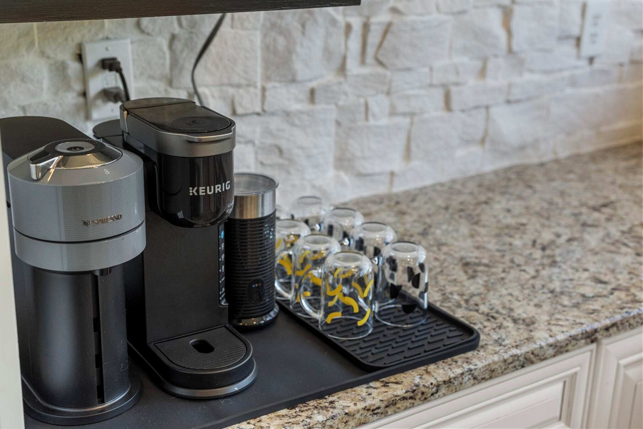 Eine Kaffeemaschine, eine Karaffe und ein Kaffeeautomaten auf einer Küchenarbeitsplatte mit einer Granitplatte und einer Steinwand im Hintergrund.
