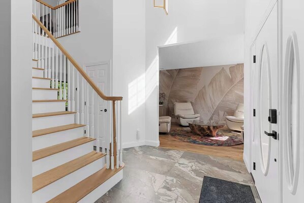 Un escalier avec des marches en bois et des rampes blanches, une porte blanche et une pièce avec un sol à motifs et une table basse.
