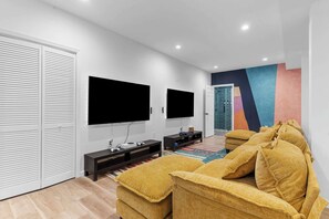 Ein modernes Wohnzimmer mit einer Couch, zwei Flachbildfernsehern, einer Anrichte und einer farbenfrohen Wand.