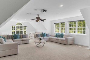 A spacious loft bedroom with a large window, a ceiling fan, and a projector.