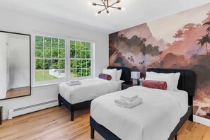 A hotel room with two beds, a large window, and a mural.