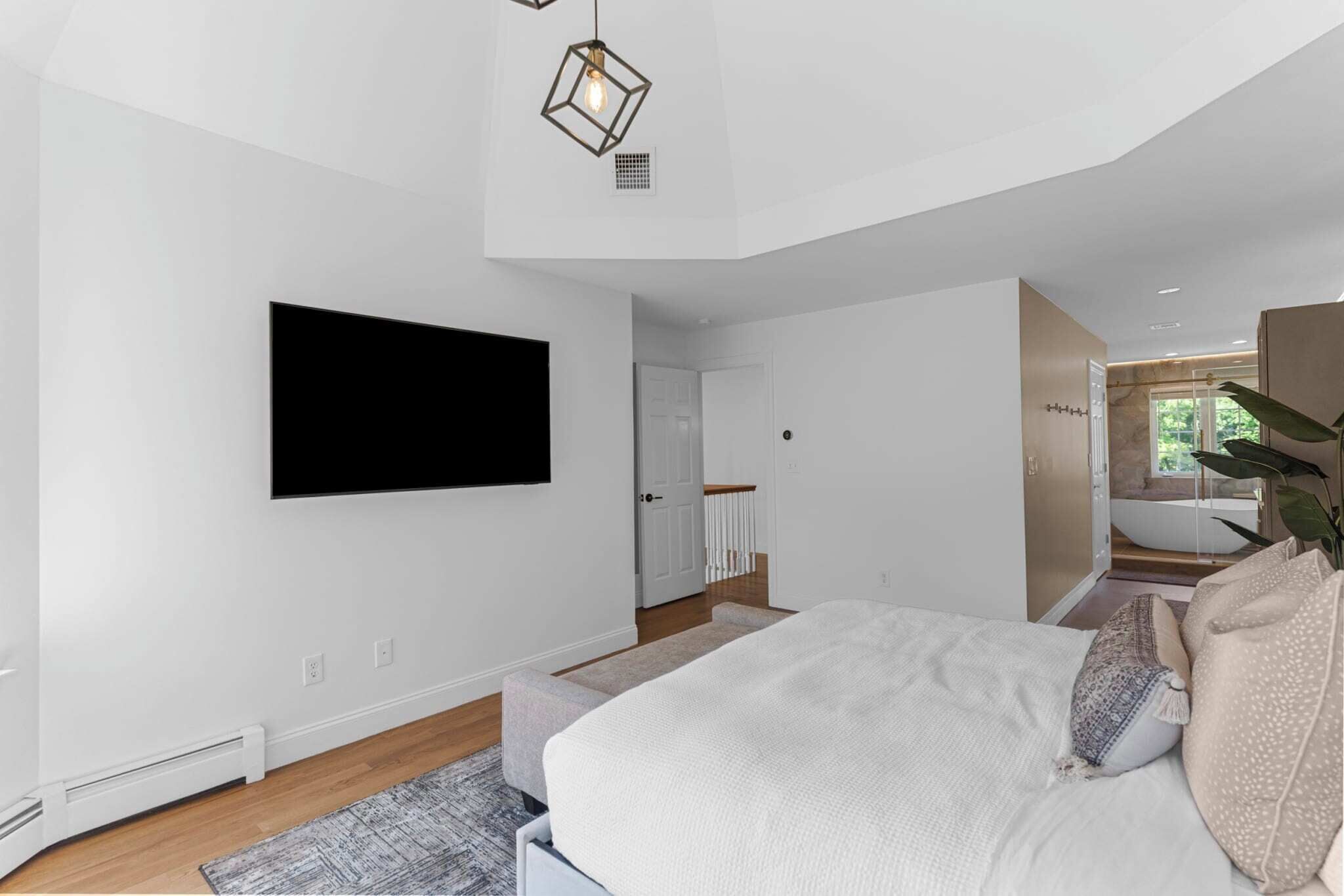 A modern bedroom with a large bed, a mounted TV, and a unique geometric light fixture.