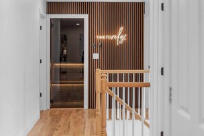 A modern interior with a wooden floor, a glass door leading to a room, and a wooden railing with a neon sign.