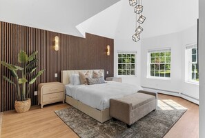 Une chambre à coucher moderne avec un lit, des tables de chevet, un banc, une plante en pot et un luminaire au design géométrique.