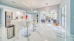 A modern kitchen with marble countertops, stainless steel appliances, and bar stools.