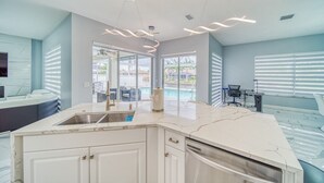 A modern kitchen with a marble countertop, a built-in sink, and a dining area with a pool view.