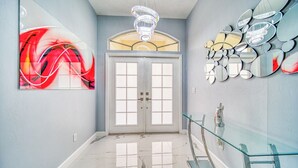 A hallway with a marble floor, a glass railing, a chandelier, and a door with frosted glass panels.