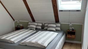 A bedroom with a sloped ceiling, a bed with striped bedding, a bedside table with a lamp, and a window with a view.
