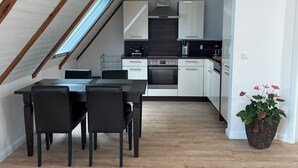 A modern kitchen with white cabinets, a black countertop, and a wooden ceiling.