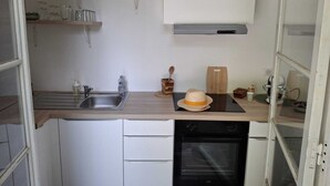 A compact kitchen with a sink, stove, and oven. There are shelves above the sink and a cutting board on the counter. - Studio rental with pool (Solliès-Pont)