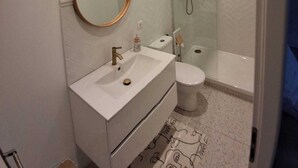A modern bathroom with a round mirror, a sink, a toilet, and a glass-enclosed shower. - Studio rental with pool (Solliès-Pont)