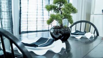 Uma mesa de jantar com uma árvore bonsai num vaso preto, rodeada por cadeiras pretas com almofadas brancas.