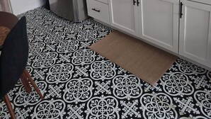 Une cuisine compacte dotée d’un réfrigérateur en acier inoxydable, de meubles blancs, d’un sol à motifs noir et blanc et d’une fenêtre laissant entrer la lumière naturelle.