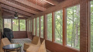 Une cabane en bois dotée de grandes fenêtres, de meubles en osier et d’un ventilateur de plafond.